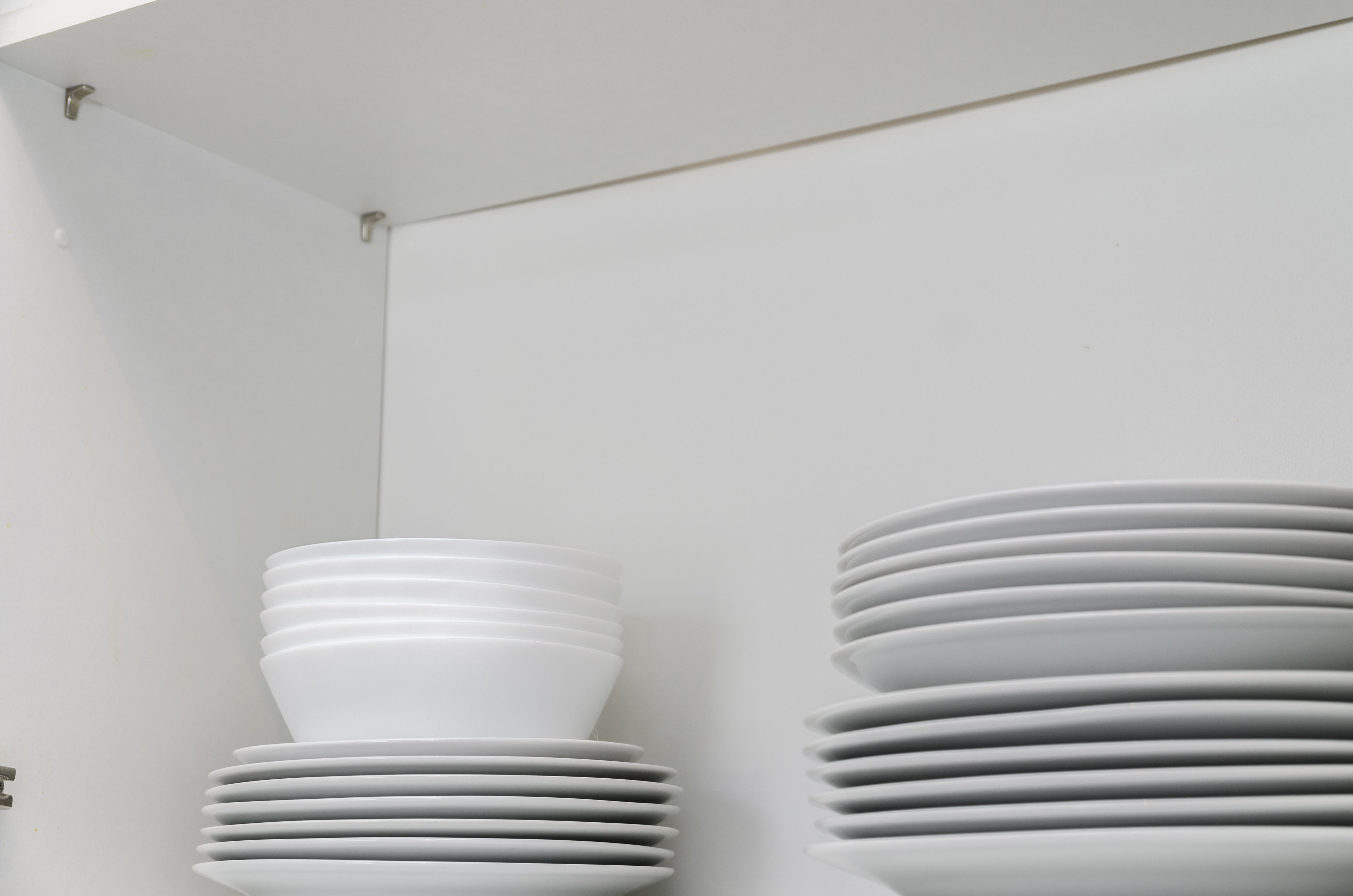 A stack of white plates against a white wall.