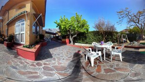 Un patio con suelo de piedra, mobiliario exterior y un edificio con un ventanal grande.