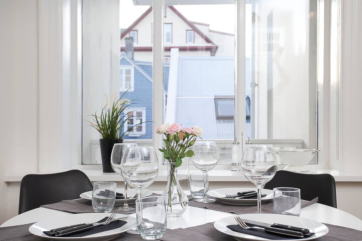 A dining table set for two with a vase of flowers, clear glasses, and cutlery.