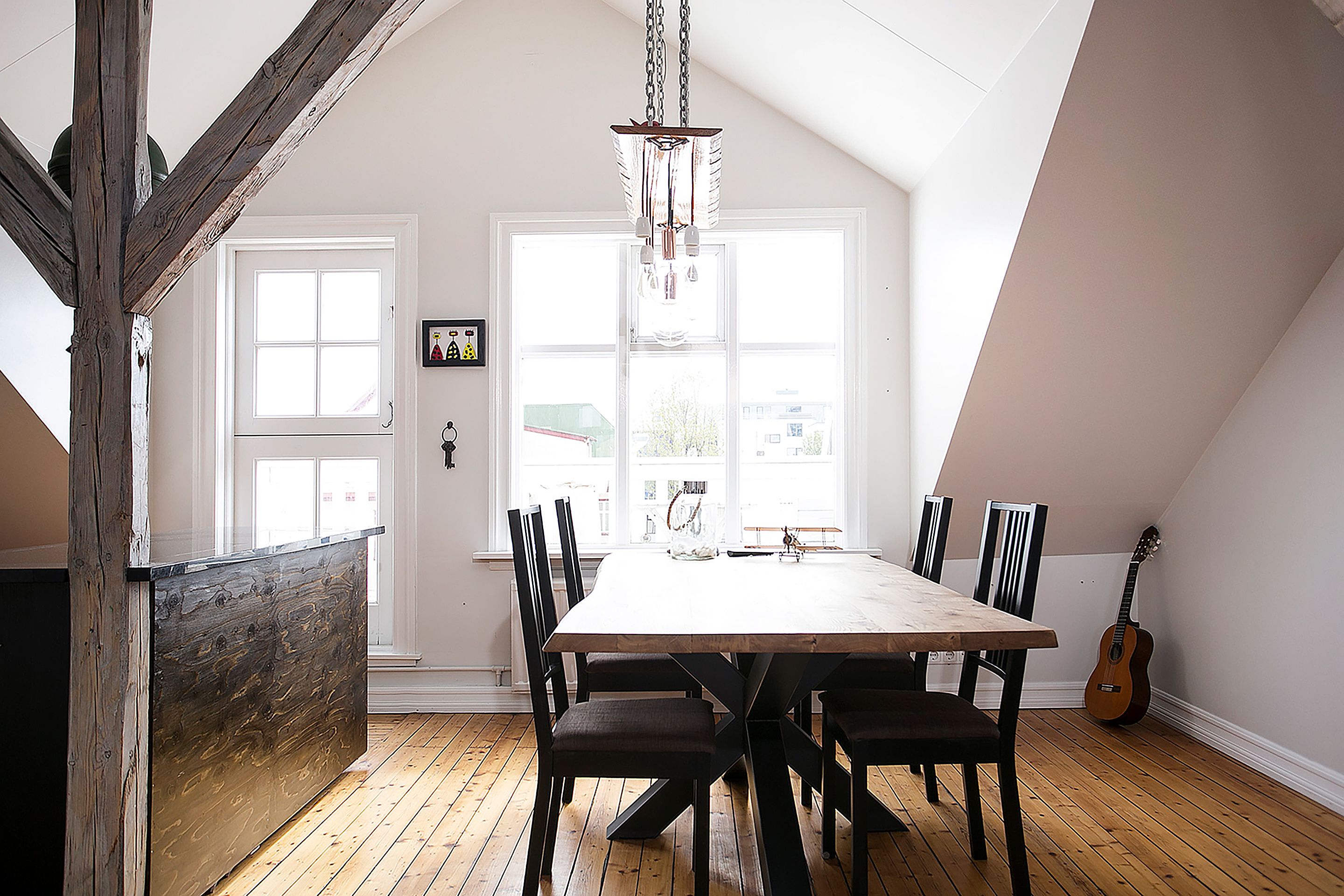 A dining area with a wooden table and chairs, a chandelier, and a guitar against the wall.