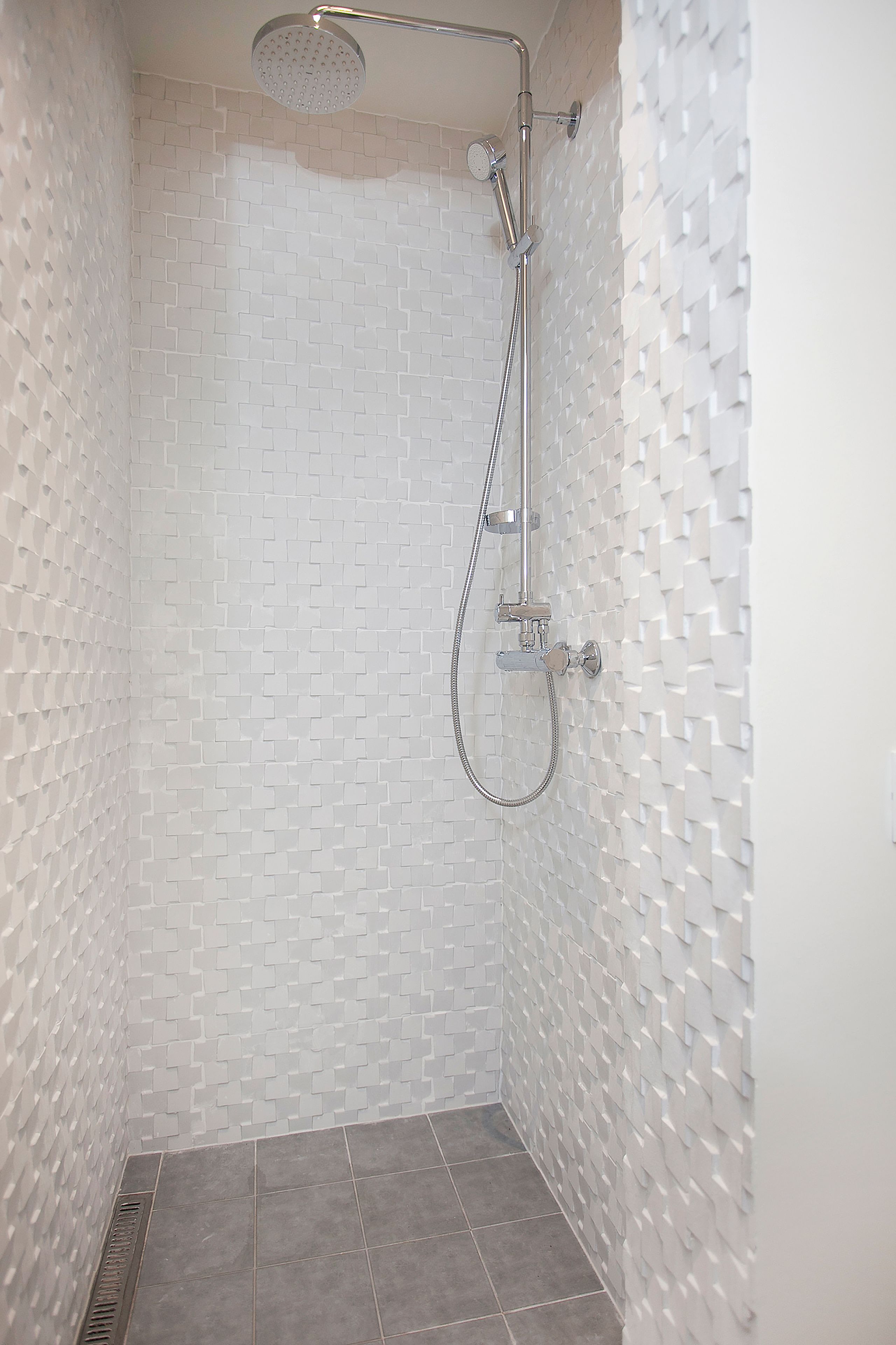 Een douche met modern design, met een witte betegelde wand en douchekop.