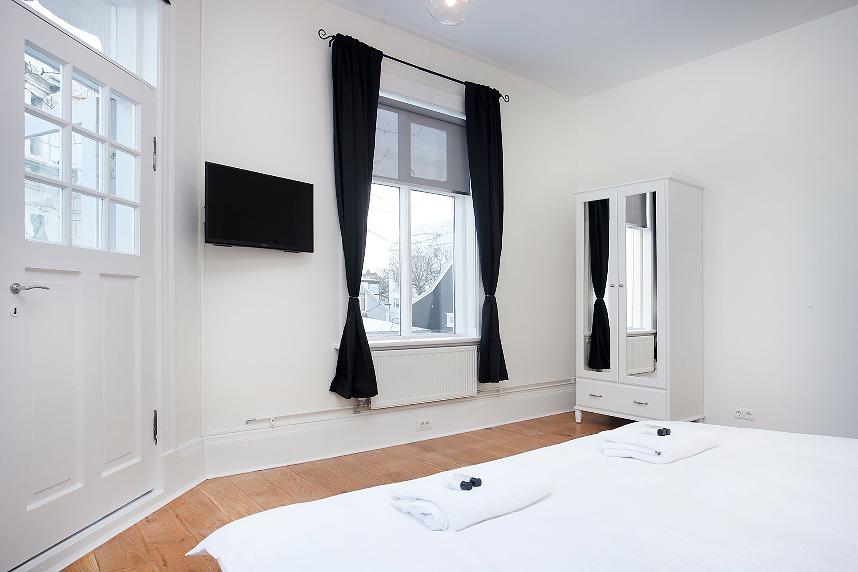 A hotel room with a large bed, a wardrobe, a television, and a window with curtains.