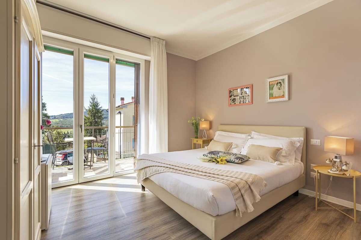 A bedroom with a large bed, a sliding glass door to a balcony, and a small bedside table with a lamp.