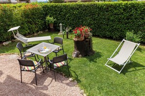 Un patio con mesa y sillas, una silla de lounge y plantas en macetas.