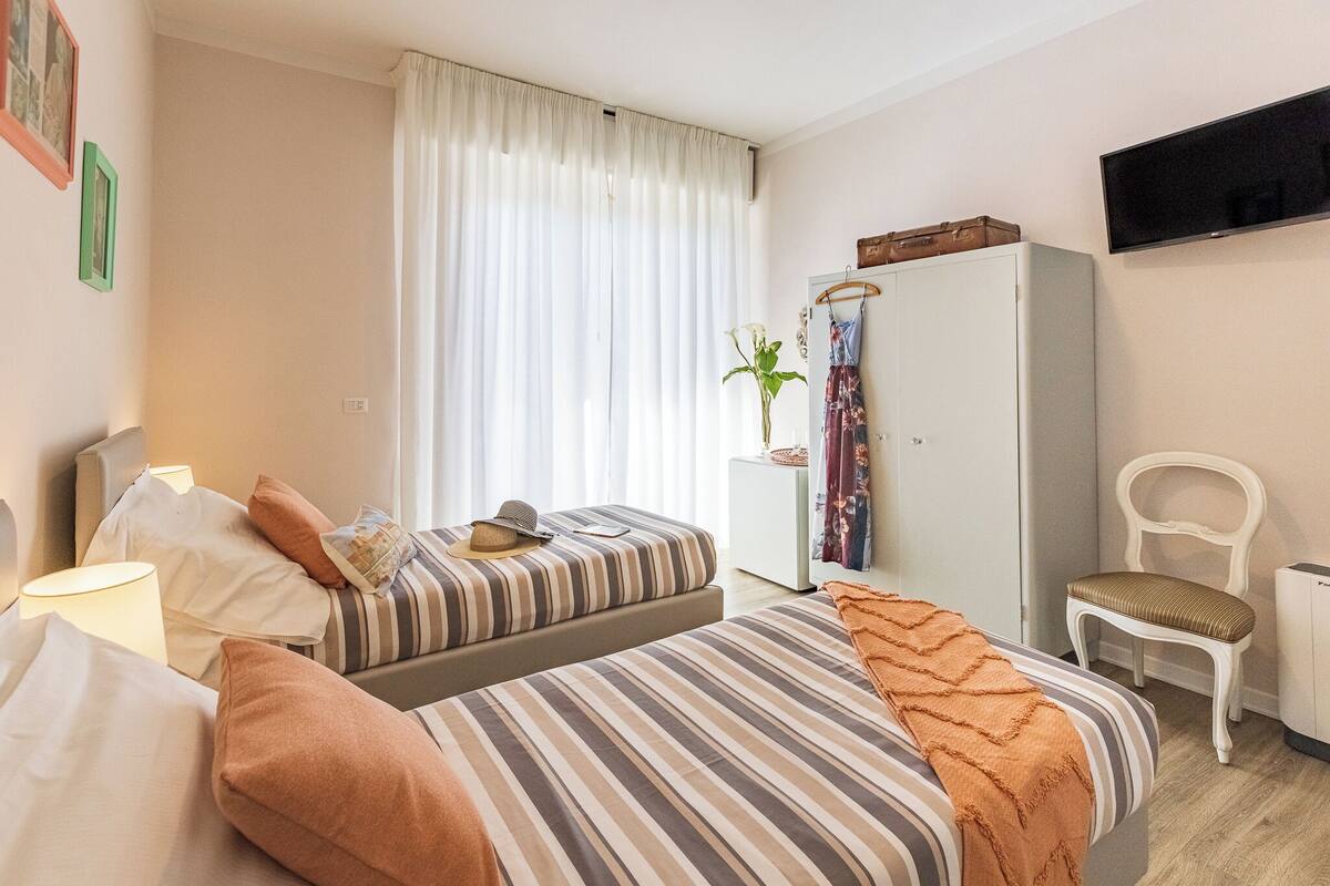 A hotel room with two beds, a wardrobe, a TV, and a chair.