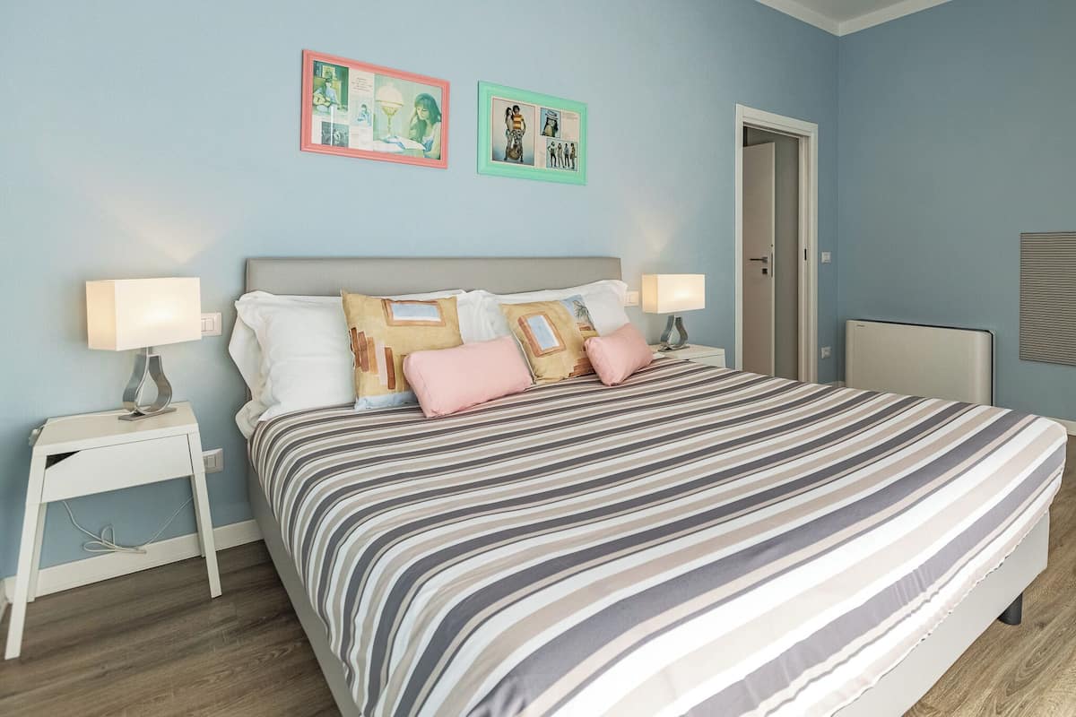 A bedroom with a large bed, two bedside tables with lamps, and two framed pictures on the wall.