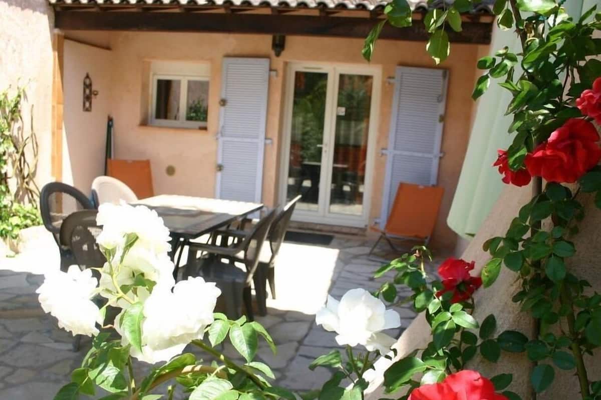 Une terrasse extérieure avec une table et des chaises, une porte avec des panneaux de verre et un mur percé d’une porte.