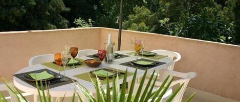 Un espace de restauration en plein air avec des tables disposées pour deux personnes, chacune agrémentée d’un chemin de table vert, d’assiettes blanches et de verres transparents.
