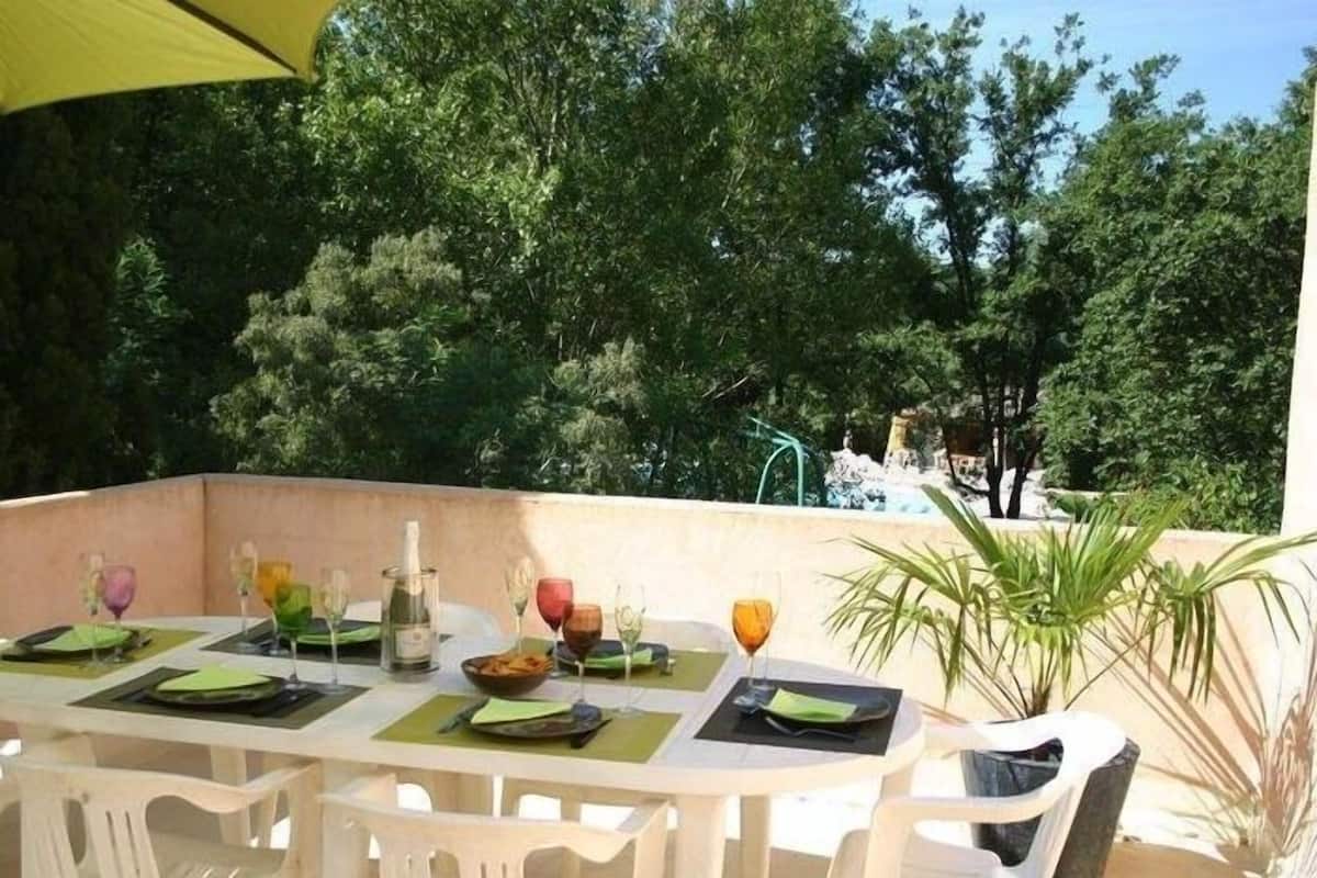 Un espace de restauration en plein air avec des chaises et des tables en plastique blanc, des sets de table verts et divers verres et bouteilles.