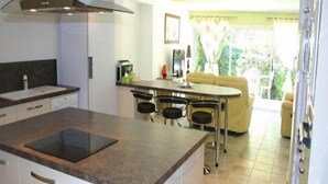 Uma cozinha moderna com uma ilha central, uma área de jantar com um sofá amarelo e vista para o verde lá fora.