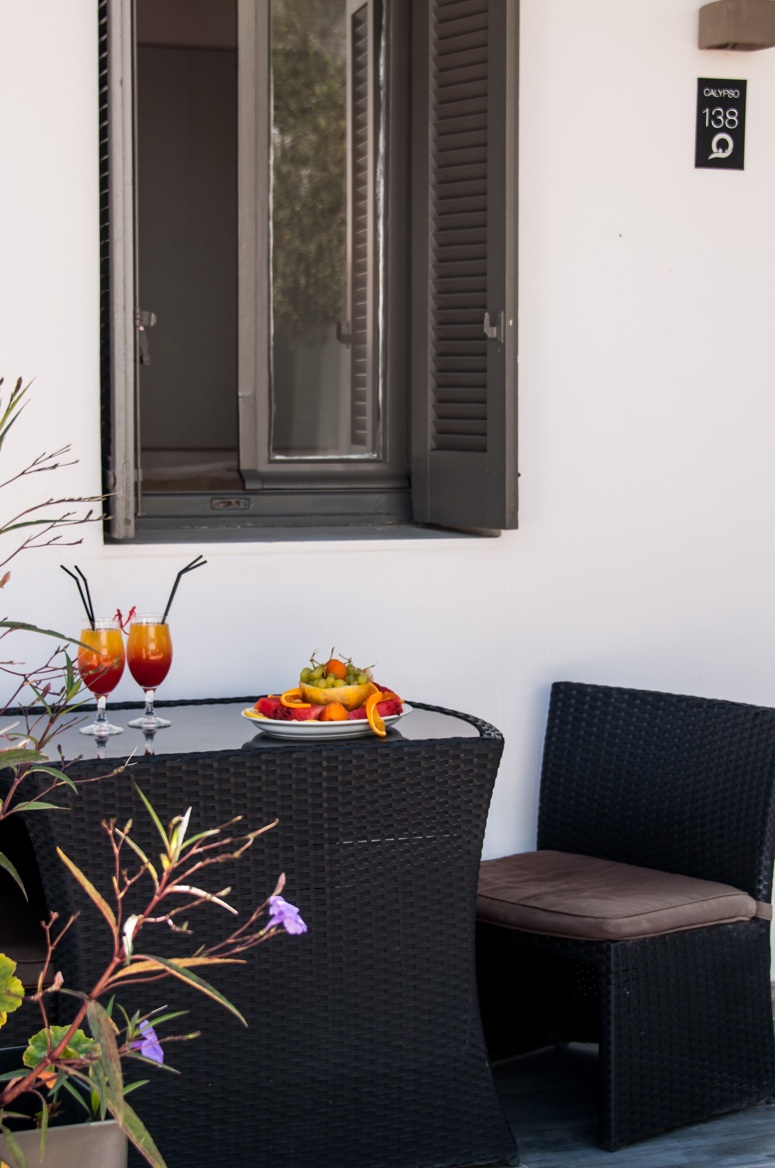 A table with two drinks, a fruit plate, and a wicker chair.