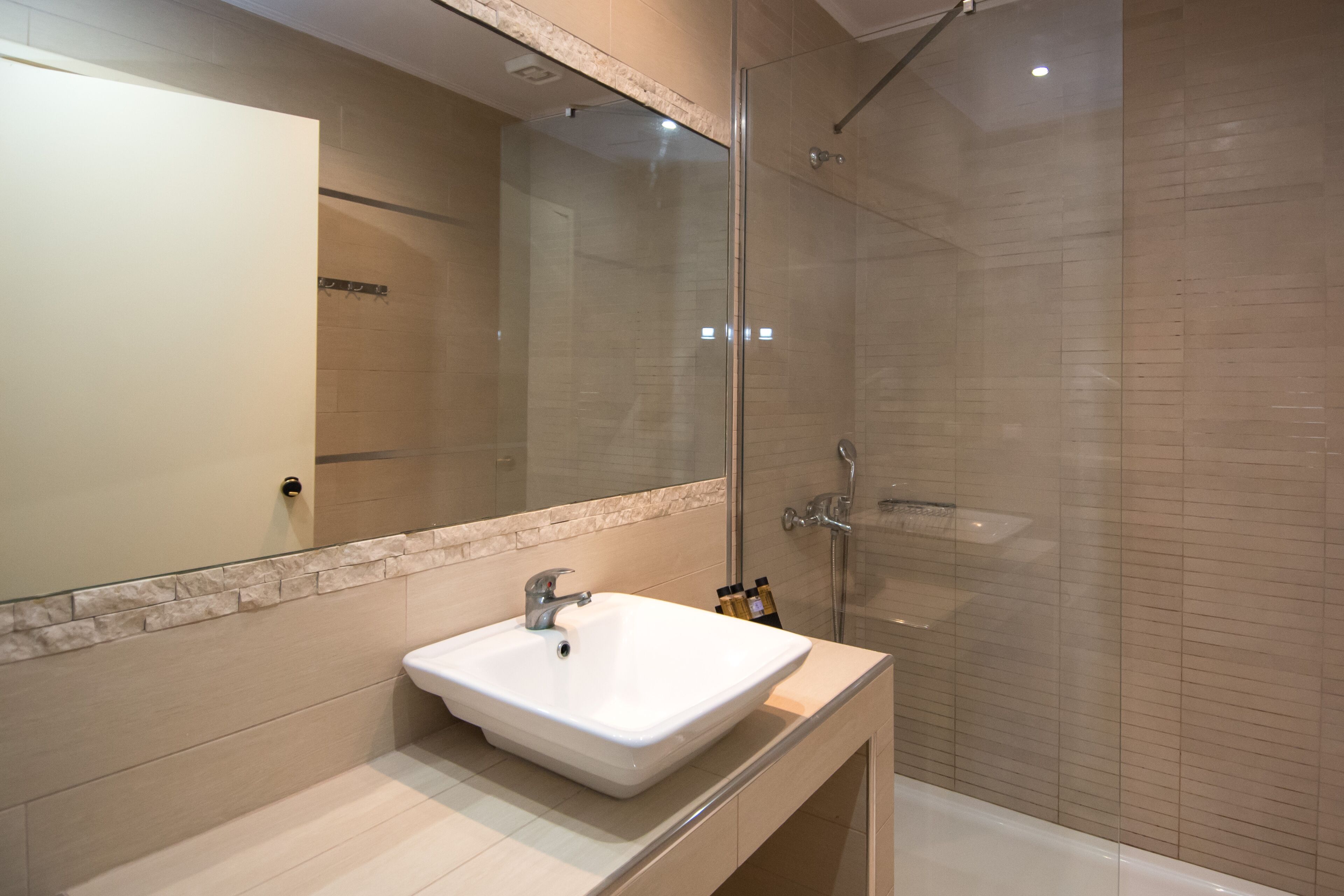 Een moderne badkamer met een douchecabine van glas, een witte wastafel en een grote spiegel.