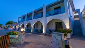 A modern building with multiple balconies, outdoor seating, and a well-lit entrance. - Sunny Garden (Zakynthos)