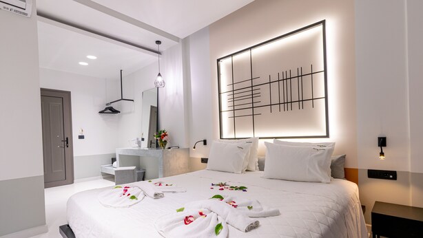 A modern hotel room with a large bed, a bedside table, a mirror, and a wall-mounted light fixture. - Sunny Garden (Zakynthos)