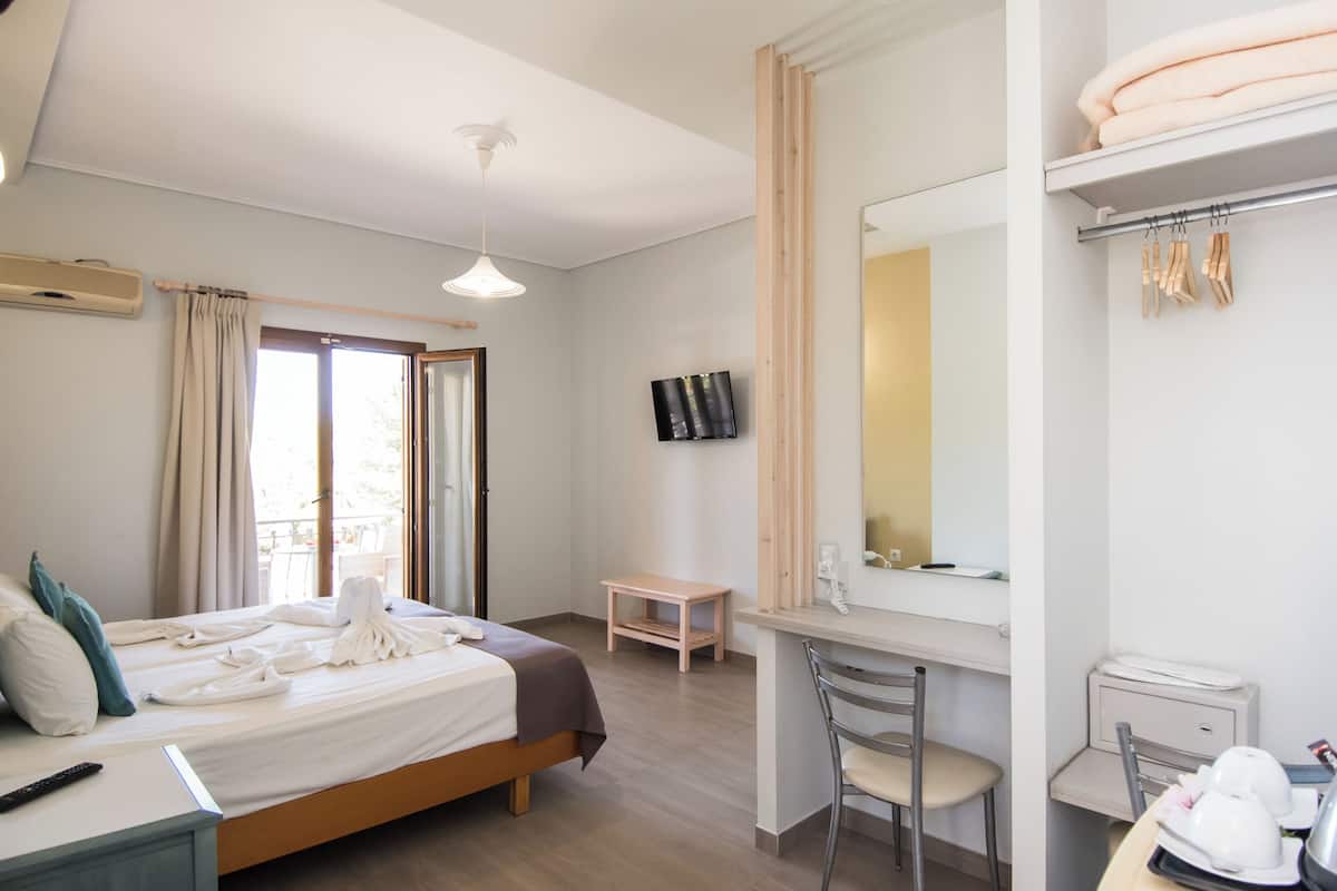 Ett hotellrum med en säng, ett skrivbord, en stol och ett badrum med en spegel och en handduksställning.