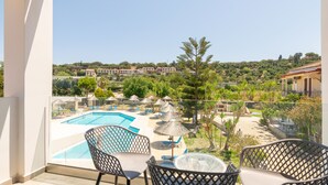 A balcony with a pool view, outdoor seating, and a view of a resort area. - Sunny Garden (Zakynthos)