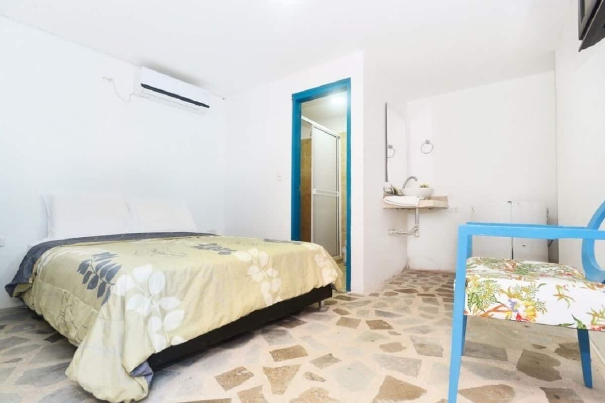 A small, clean room with a bed, a chair, a bathroom with a sink, and a shower.