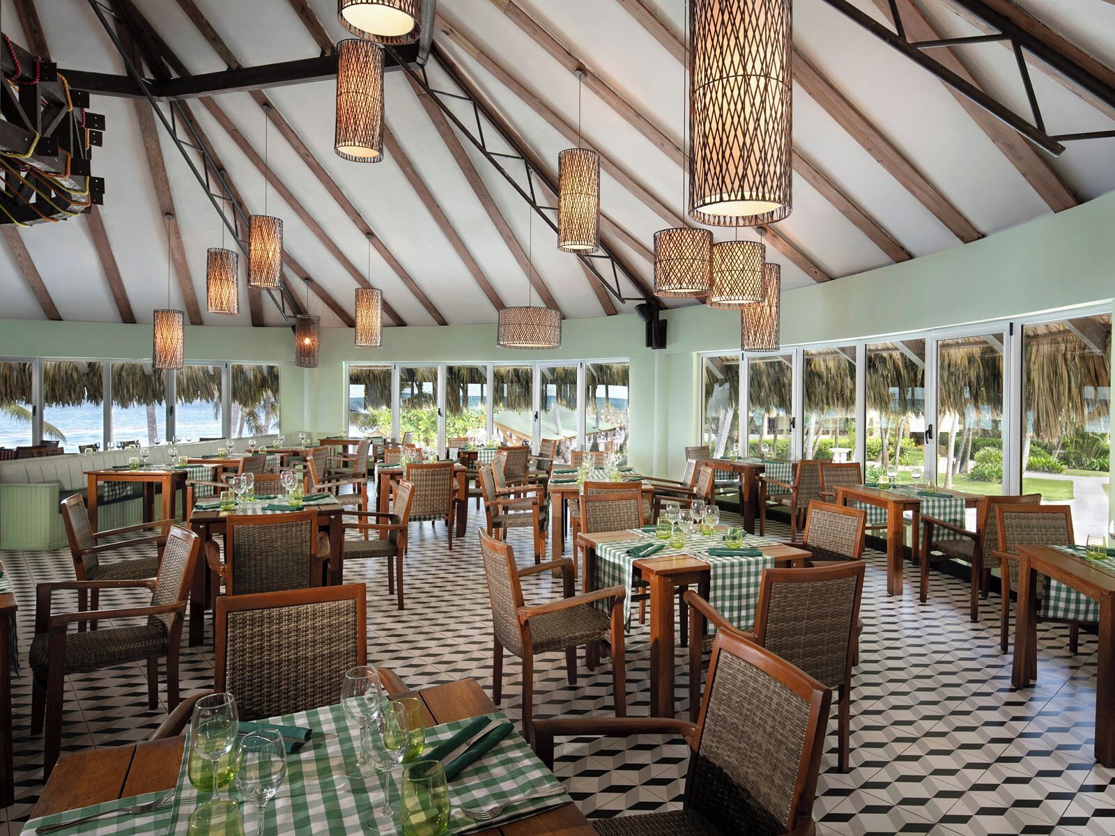 A restaurant with checkered tablecloths, wicker chairs, and hanging wicker lamps.