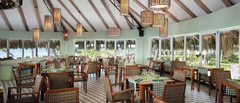 A restaurant with checkered tablecloths, wicker chairs, and hanging wicker lamps.