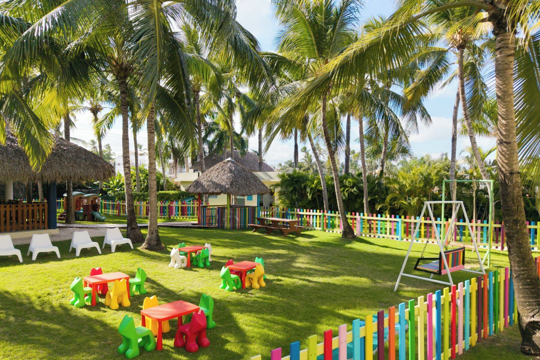 Um resort tropical com chalés de palha, estruturas de recreação coloridas e baloiço.