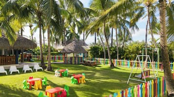 Um resort tropical com chalés de palha, estruturas de recreação coloridas e baloiço.