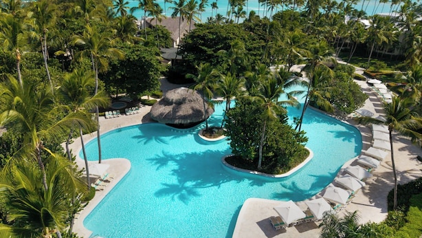 Ein Hotelpool in tropischer Umgebung, umgeben von Palmen und mit Blick auf den Ozean.