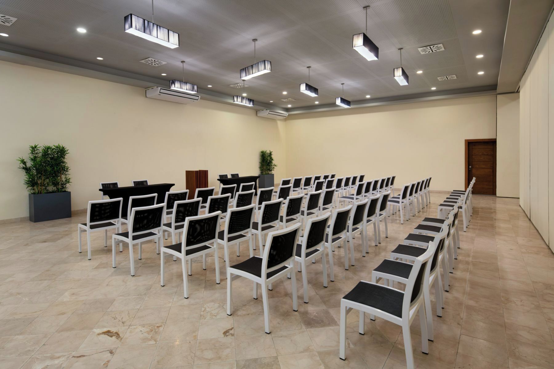 Un salón de conferencias con filas de sillas blancas, un atril y luces en el techo.
