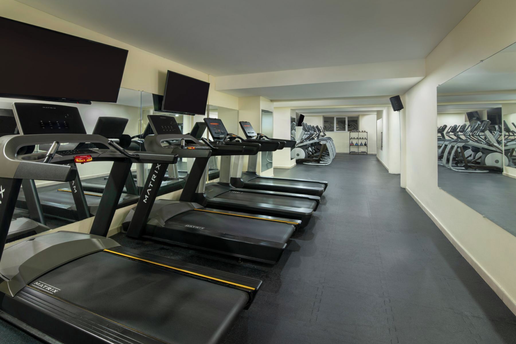 Ein Fitnessstudio mit mehreren Laufbändern, Ergometer und einer Spiegelwand.