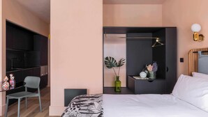 A modern hotel room with a bed, bedside table, chair, and a small desk area with a chair.