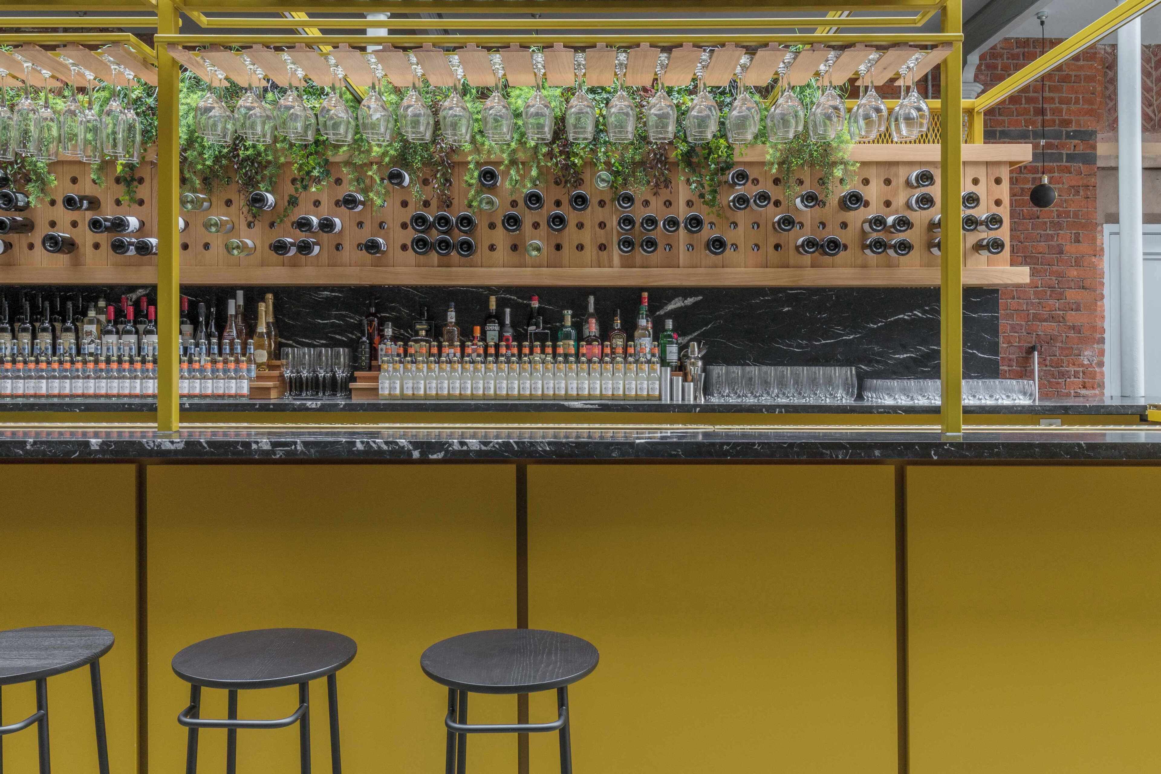 A bar area with a wine rack, stools, and a yellow wall.