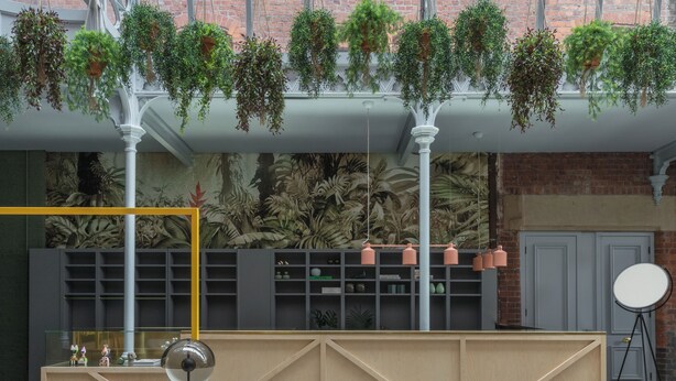 A modern interior with hanging plants, a brick wall, and a wooden reception desk.