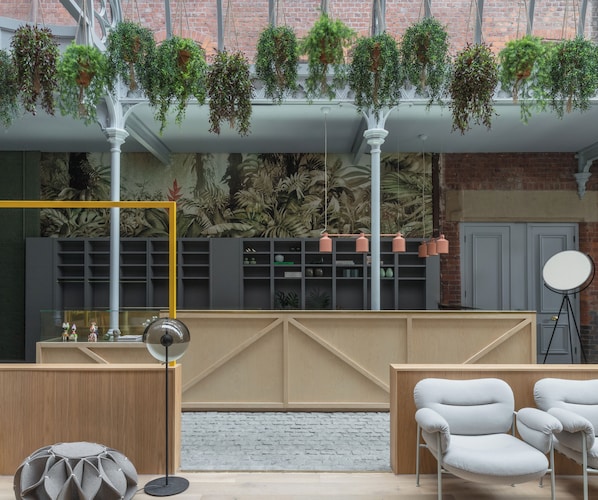 A modern interior with hanging plants, a brick wall, and a wooden reception desk. - Whitworth Locke (Manchester)