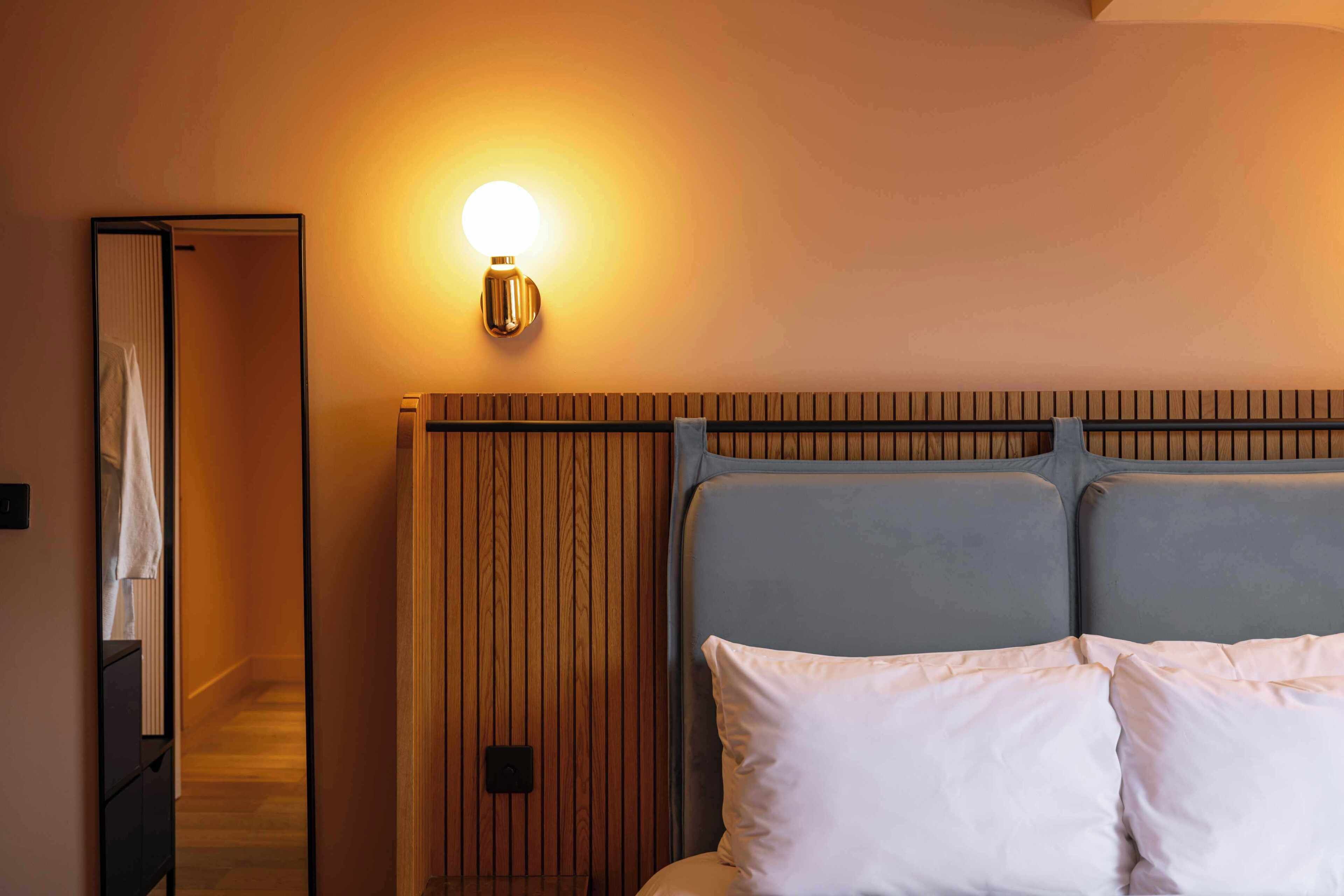 A hotel room with a bed, a wooden headboard, a wall-mounted light, and a mirror.