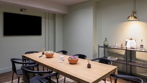 A conference room with a long table, chairs, a flat-screen TV, a shelf with glassware, and a pendant light.