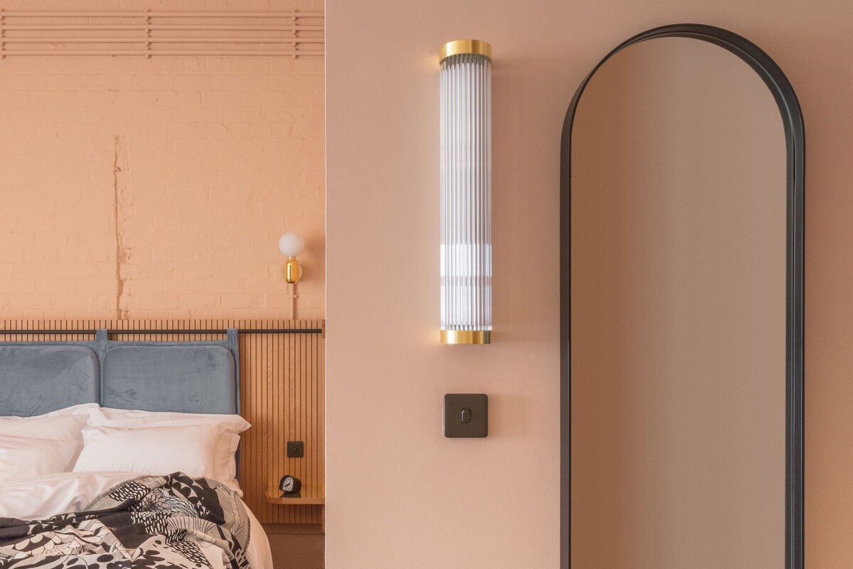 A bedroom with a bed, a wall-mounted light fixture, a clock, and a mirror.