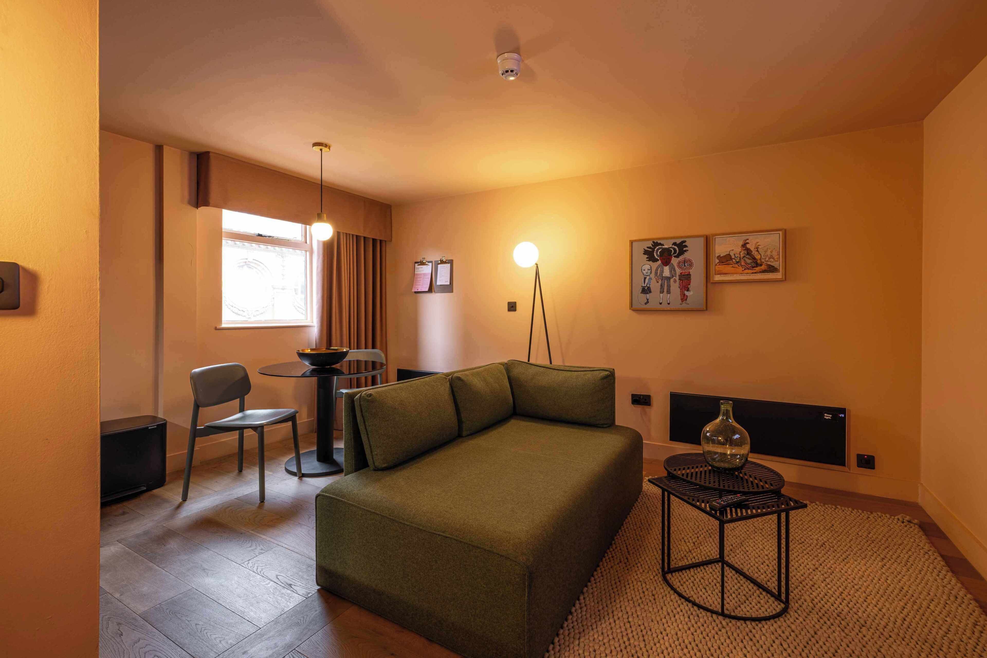 Une pièce confortable avec un canapé, une petite table, une chaise et une lampe.