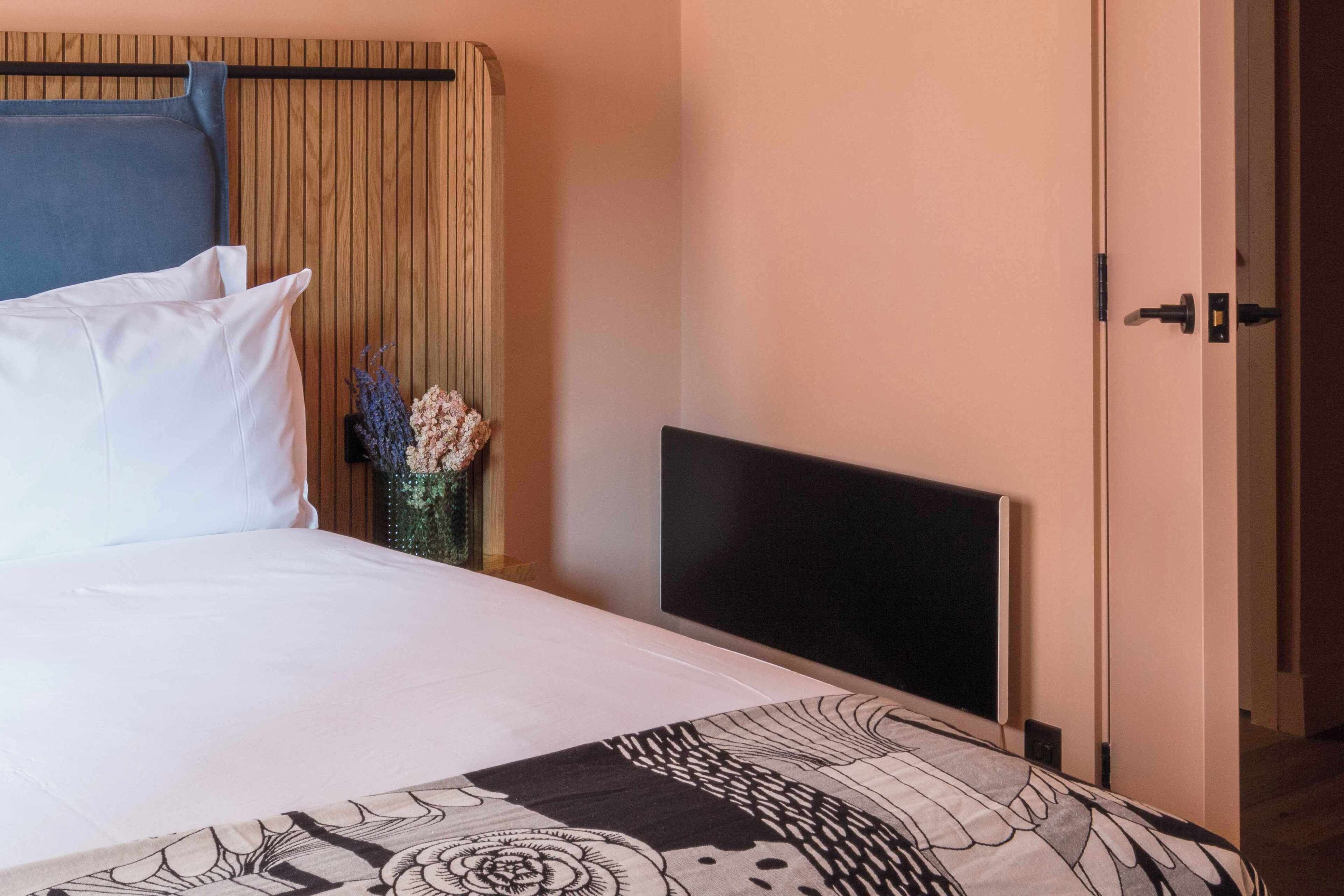 A hotel room with a bed, a flat-screen TV, a wooden headboard, and a door.