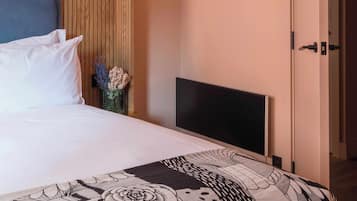 A hotel room with a bed, a flat-screen TV, a wooden headboard, and a door.