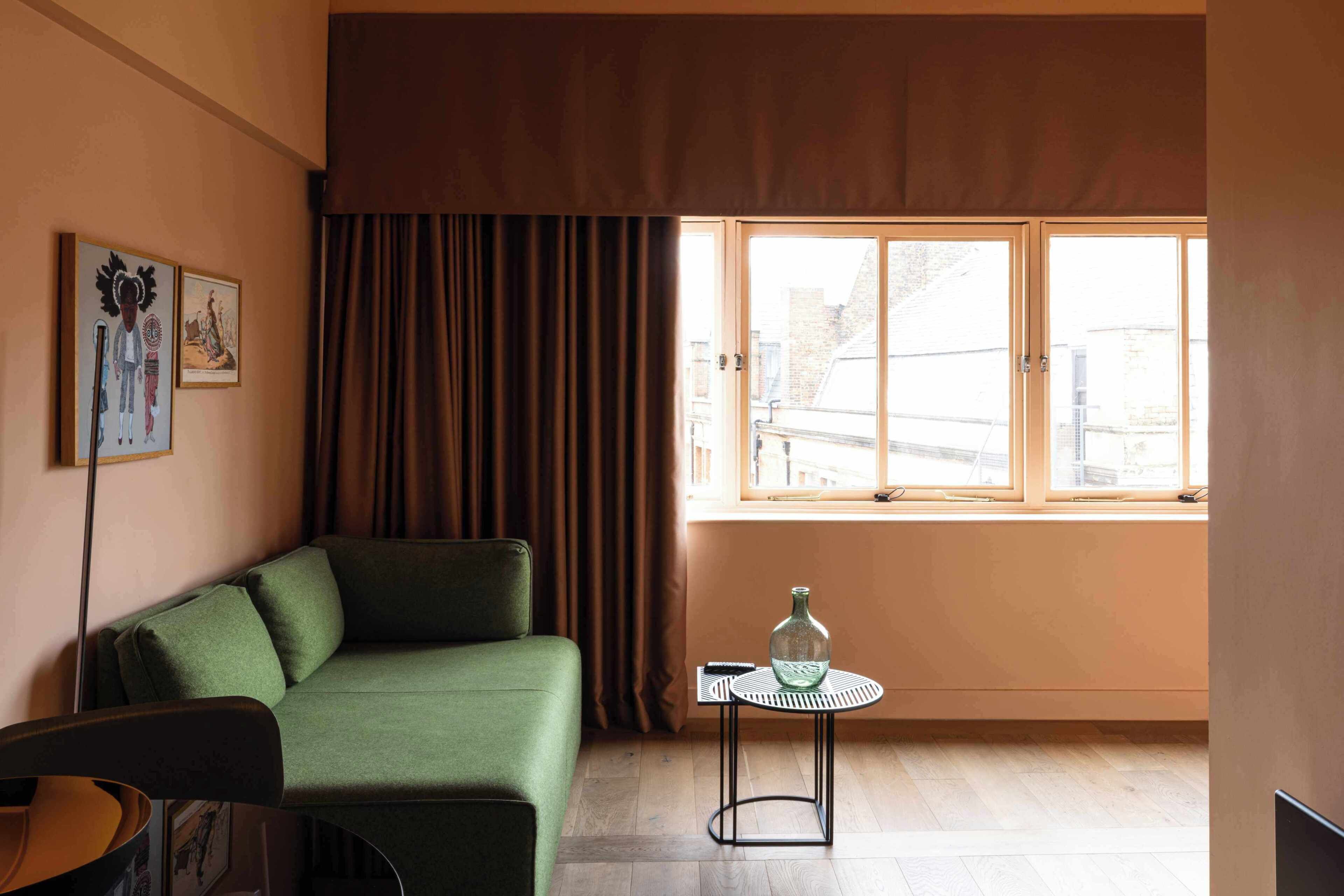 A room with a green sofa, a small round table with a bottle, a chair, and a window with curtains.