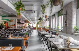 Un restaurante con techos altos, plantas colgantes, paredes de ladrillo y una variedad de arreglos de asientos, incluidas mesas y cabinas.