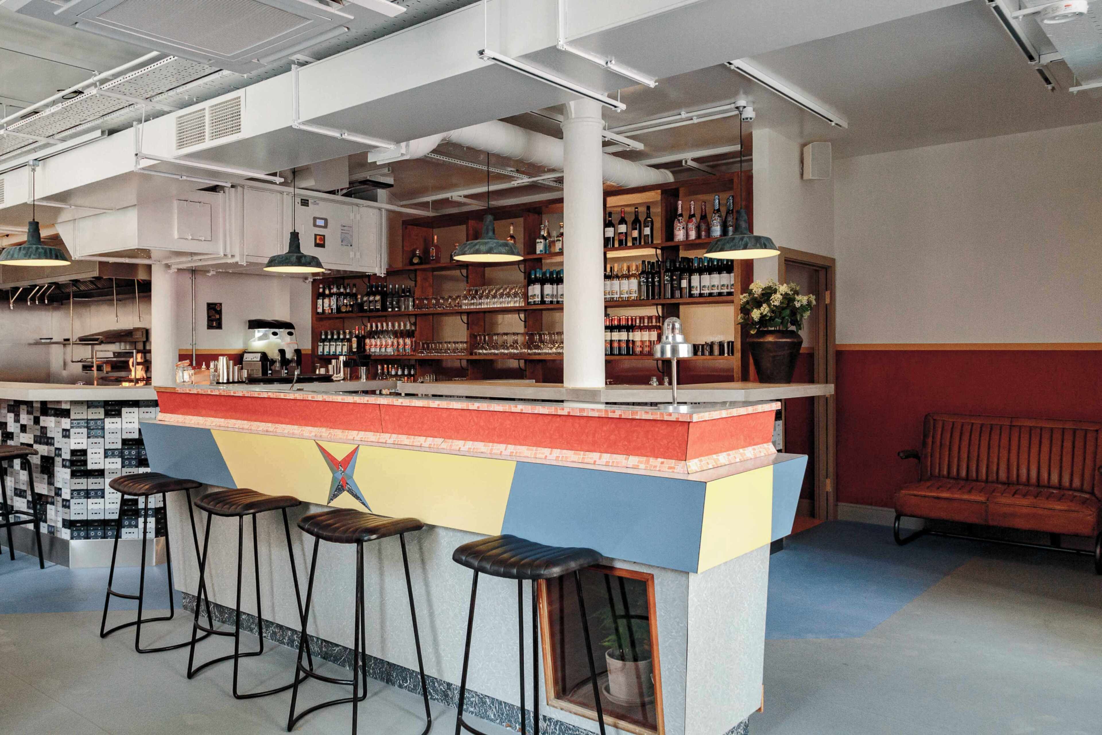 Un espace bar avec des tabourets, des étagères remplies de bouteilles et une plante en pot.