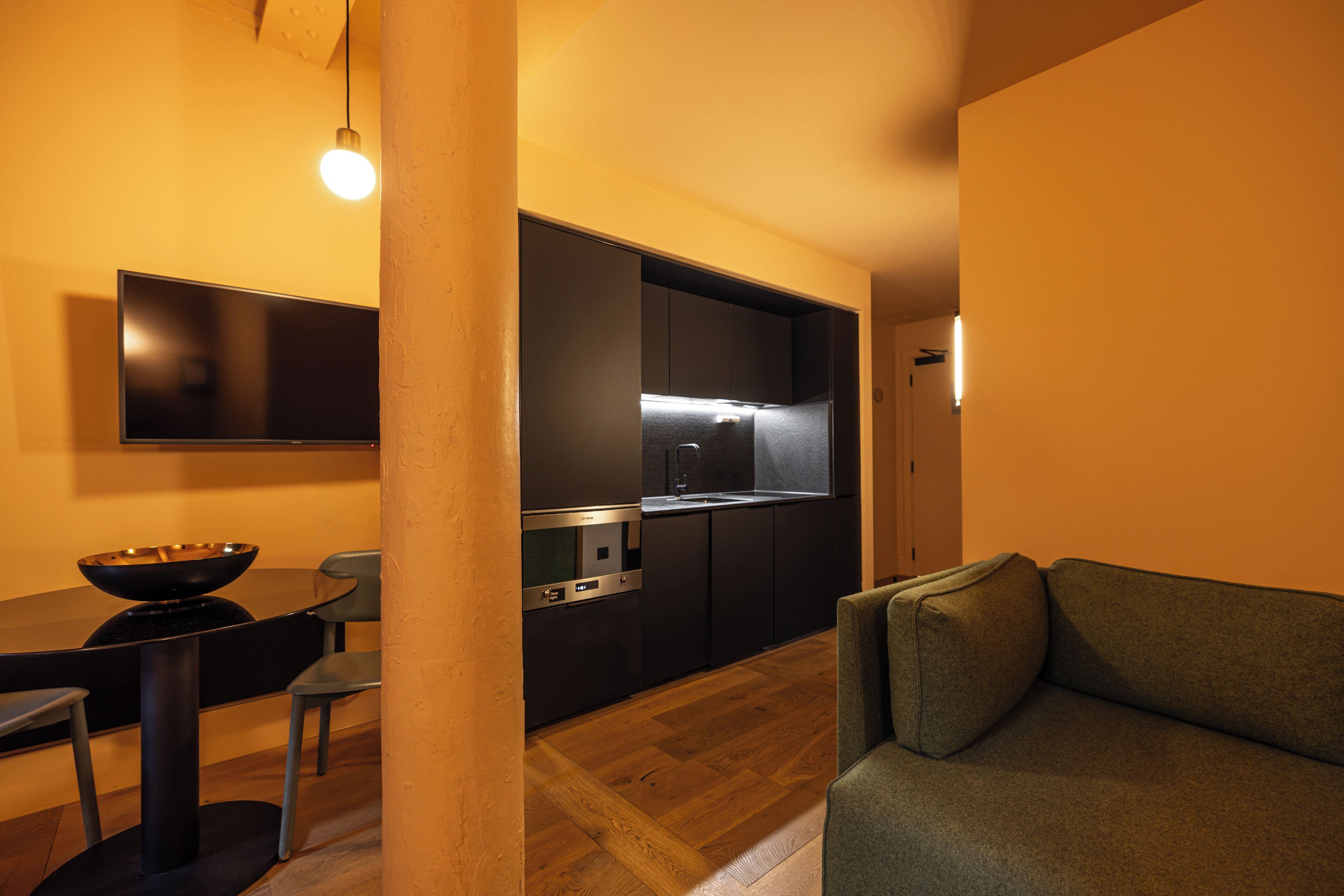 A modern kitchen with dark cabinetry, a built-in oven, and a dining area with a table and chairs.
