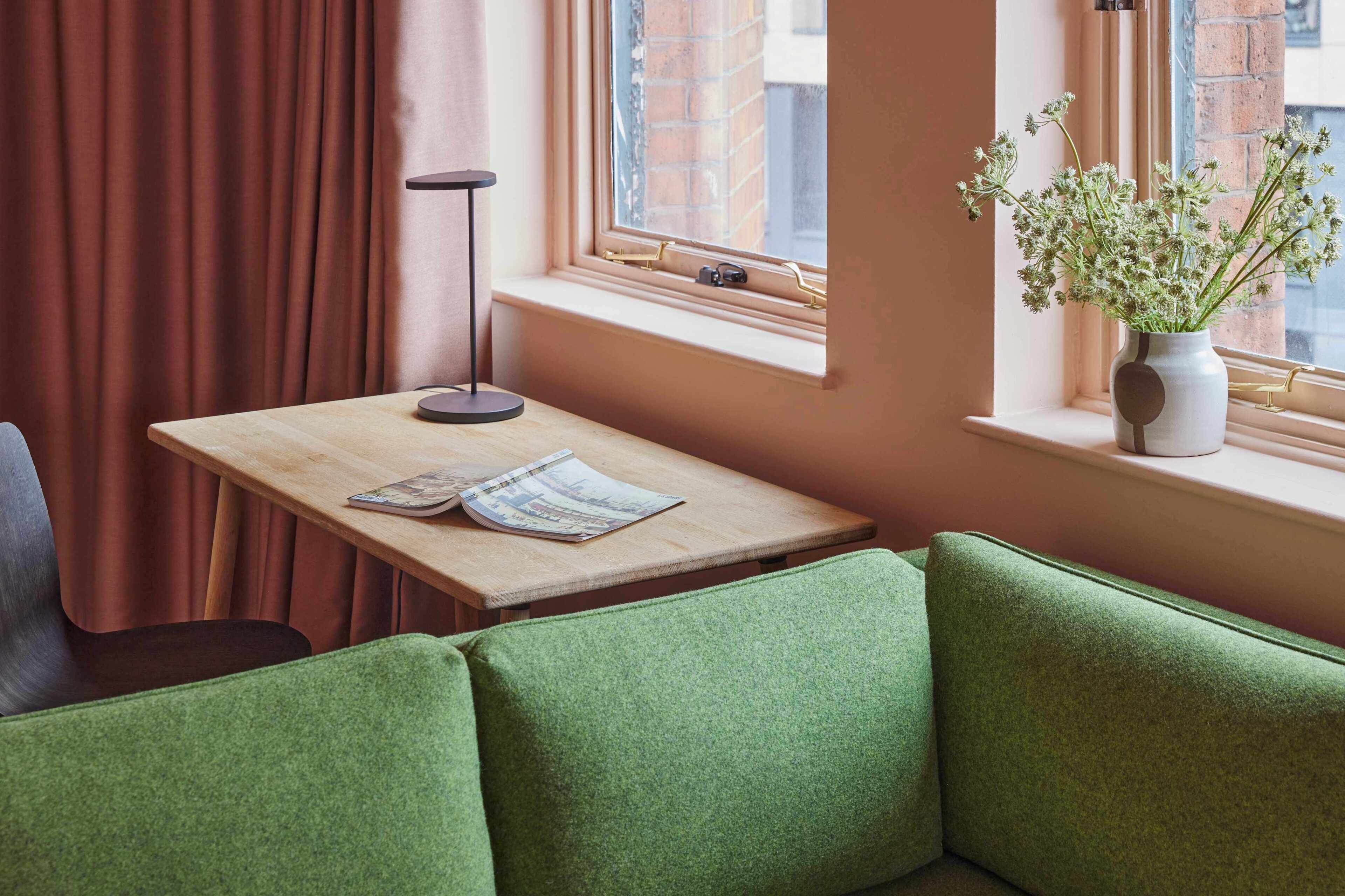 A cozy seating area with a wooden table, a vase with flowers, and a window with a view of a brick building.