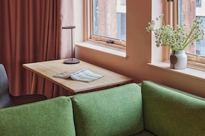 Un rincón acogedor con una mesa de madera, un jarrón con flores y una ventana que ofrece vistas a un edificio de ladrillo.