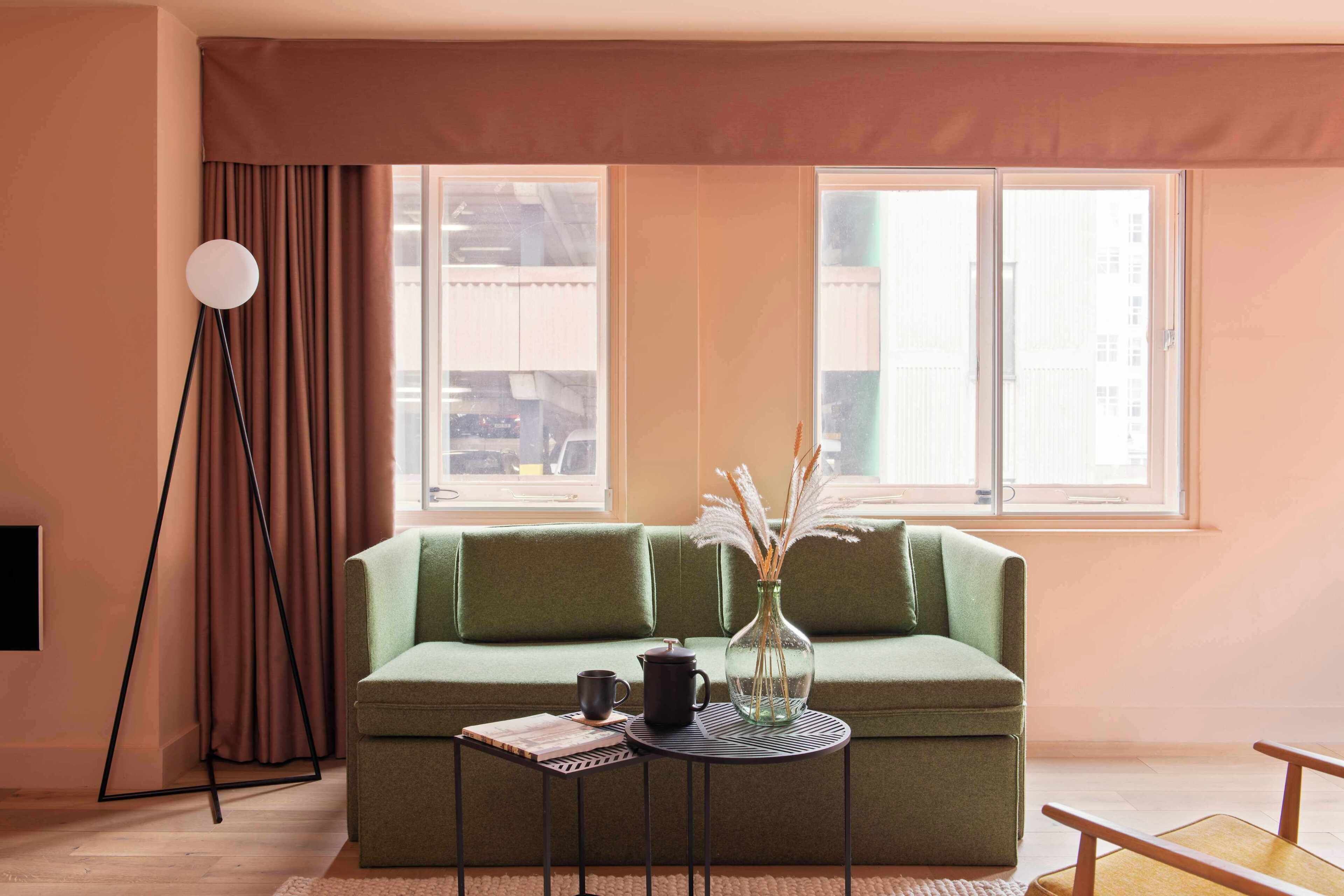 A green sofa, a small round table with a vase, a floor lamp, and a window with curtains.