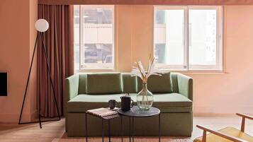 A green sofa, a small round table with a vase, a floor lamp, and a window with curtains.