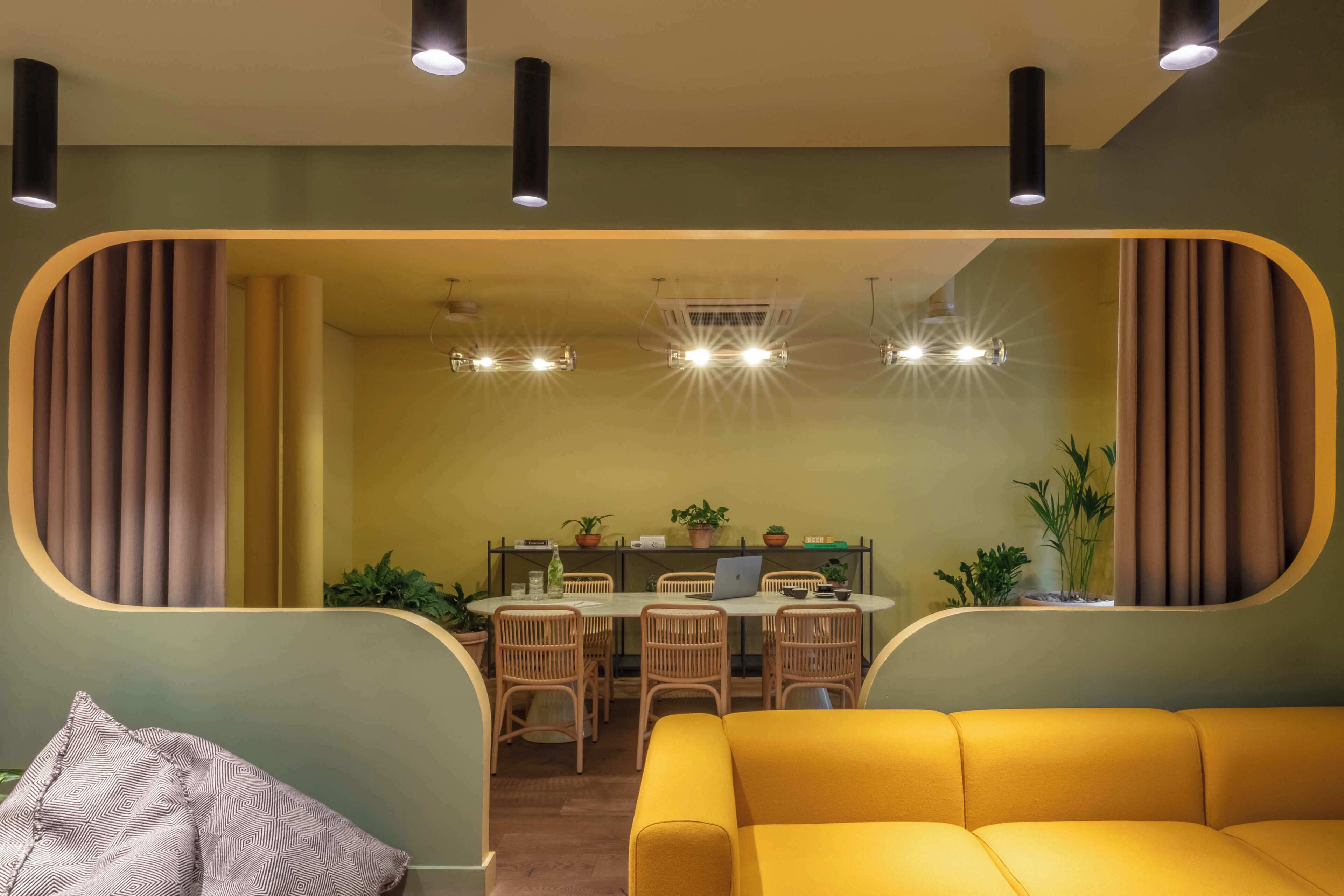 Ein modernes Interieur mit einem gelben Sofa, einer Essecke mit Stühlen und einem Tisch sowie einer Küche im Hintergrund.