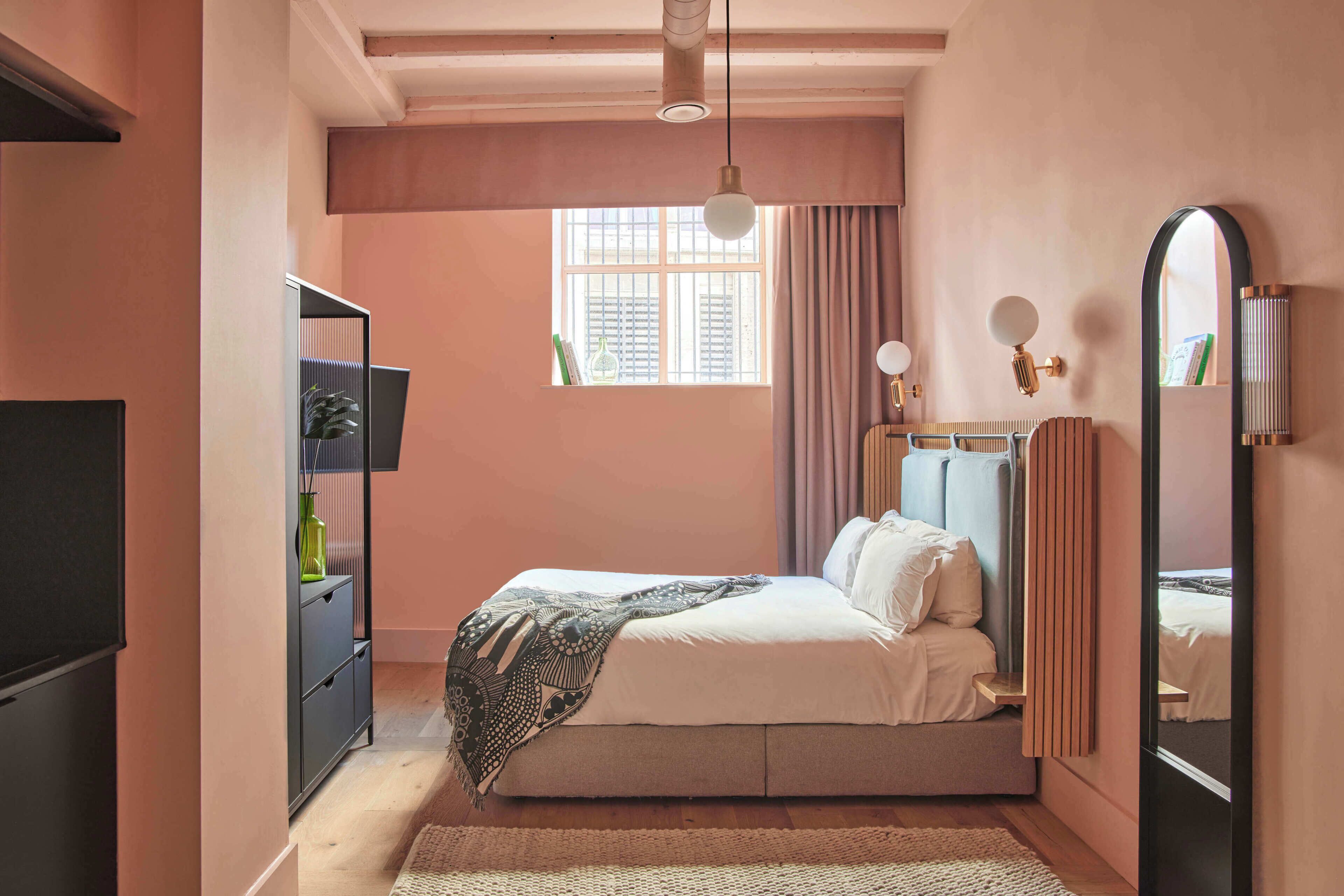 A bedroom with a bed, a bedside table, a mirror, a window, and a wardrobe.
