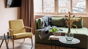 A living room with a sofa, armchair, TV, and a window with a view of buildings.
