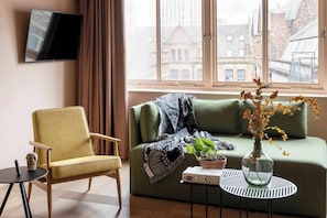 A living room with a sofa, armchair, TV, and a window with a view of buildings. - Whitworth Locke (Manchester)
